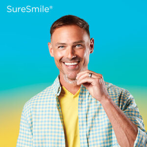 SureSmile® Clear Aligners glad kille som håller i en SureSmile i handen. Blågul bakgrund.